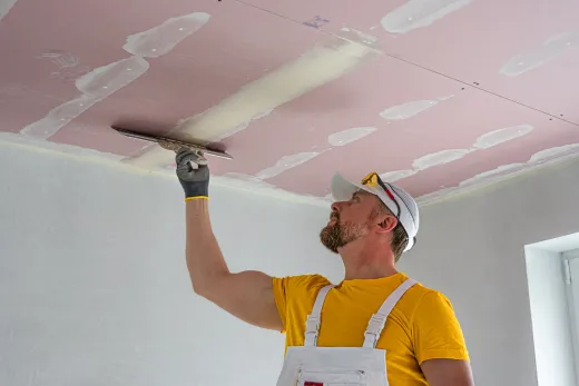 Tradesperson taping a drywalled ceiling and bulkhead during a basement renovation