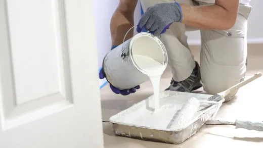 Painter pouring a deep-toned paint into a tray — prep for a colour-drenched room