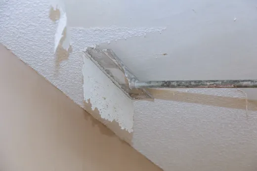 Worker scraping textured popcorn coating off a ceiling during a GTA renovation